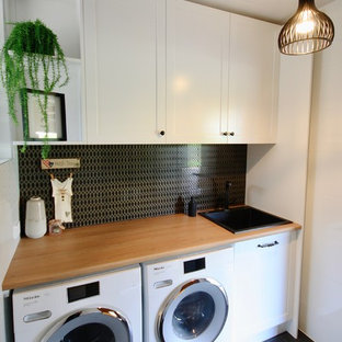 Réalisation d'une petit buanderie linéaire style shabby chic dédiée avec un évier posé, un placard à porte shaker, des portes de placard blanches, un plan de travail en bois, un mur blanc, un sol en carrelage de céramique, des machines côte à côte et un sol noir.