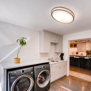 Idéer för att renovera en mellanstor funkis u-formad tvättstuga enbart för tvätt, med luckor med upphöjd panel, beige skåp, bänkskiva i kvarts, vita väggar, ljust trägolv, en tvättmaskin och torktumlare bredvid varandra, beiget golv och en undermonterad diskho