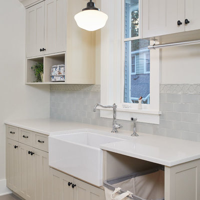 Example of a country single-wall brown floor dedicated laundry room design in Grand Rapids with a farmhouse sink, shaker cabinets, beige cabinets, white countertops, solid surface countertops and gray walls
