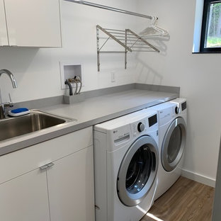 Idée de décoration pour une buanderie parallèle minimaliste dédiée et de taille moyenne avec un placard à porte plane, des portes de placard blanches, un mur blanc, un sol en vinyl, des machines côte à côte et un plan de travail gris.