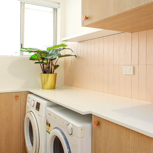 Inredning av en liten vita linjär vitt tvättstuga enbart för tvätt, med släta luckor, skåp i ljust trä, bänkskiva i kvarts, rosa stänkskydd, stänkskydd i keramik, gula väggar, vinylgolv, en tvättmaskin och torktumlare bredvid varandra och rosa golv