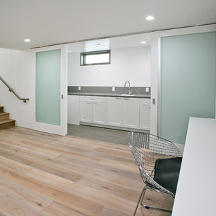 Cette photo montre une grand buanderie linéaire tendance multi-usage avec un mur blanc, un sol en bois clair, un évier encastré, un placard avec porte à panneau encastré, des portes de placard blanches, un plan de travail en stéatite et des machines superposées.
