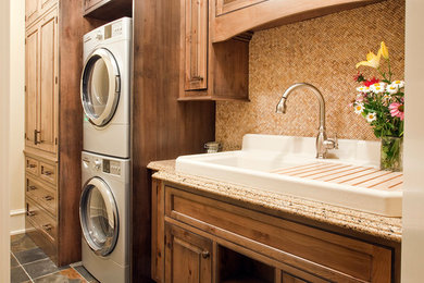Elegant single-wall dedicated laundry room photo in Chicago with granite countertops, a stacked washer/dryer, raised-panel cabinets, dark wood cabinets, a drop-in sink and beige walls