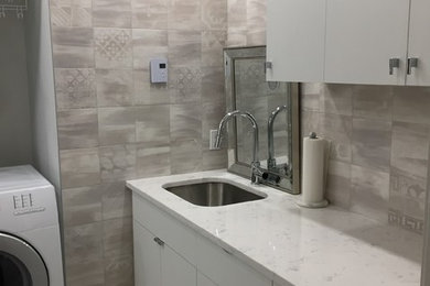Mid-sized trendy porcelain tile and gray floor laundry room photo in Montreal with an undermount sink, flat-panel cabinets, white cabinets, quartz countertops, gray walls and a side-by-side washer/dryer