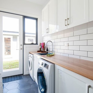 Esempio di una sala lavanderia tradizionale di medie dimensioni con ante bianche, top in legno, pareti bianche, pavimento con piastrelle in ceramica, pavimento grigio, top marrone, lavello da incasso, ante con riquadro incassato e lavatrice e asciugatrice affiancate