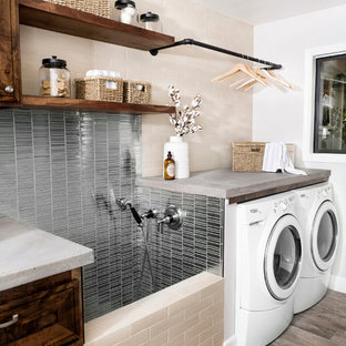 Esempio di una sala lavanderia country di medie dimensioni con lavello da incasso, ante con bugna sagomata, ante in legno bruno, top in cemento, pareti bianche, pavimento in legno massello medio, lavatrice e asciugatrice affiancate, pavimento marrone e top grigio