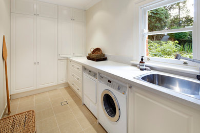 Imagen de lavadero multiusos y lineal clásico de tamaño medio con fregadero bajoencimera, puertas de armario blancas, paredes blancas y lavadora y secadora juntas