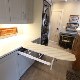 Idée de décoration pour une buanderie parallèle champêtre multi-usage et de taille moyenne avec un évier de ferme, un placard avec porte à panneau encastré, un plan de travail en granite, un mur beige, un sol en carrelage de porcelaine, des machines superposées, un sol marron, un plan de travail vert et des portes de placard grises.