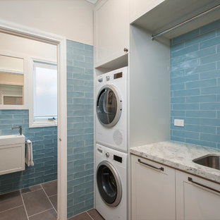 This is an example of a small transitional single-wall utility room in Melbourne with an undermount sink, shaker cabinets, beige cabinets, granite benchtops, porcelain floors, a stacked washer and dryer, grey floor, beige walls, beige benchtop and ceramic splashback.