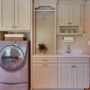 Idee per un'ampia sala lavanderia country con lavello sottopiano, ante verdi, top in quarzo composito, pareti beige, pavimento in legno massello medio, lavatrice e asciugatrice affiancate, ante con riquadro incassato, pavimento marrone e top bianco