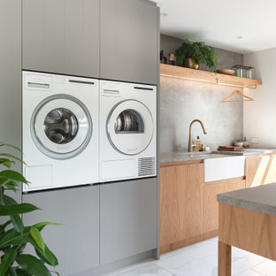 Idee per una sala lavanderia contemporanea di medie dimensioni con lavello stile country, ante lisce, ante in legno chiaro, top in quarzo composito, paraspruzzi grigio, paraspruzzi in gres porcellanato, pareti bianche, pavimento in gres porcellanato, lavatrice e asciugatrice affiancate, pavimento bianco e top grigio