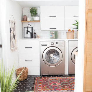Immagine di una piccola sala lavanderia minimalista con lavello sottopiano, ante lisce, ante bianche, top in quarzo composito, pareti bianche, pavimento con piastrelle in ceramica, lavatrice e asciugatrice affiancate e pavimento nero