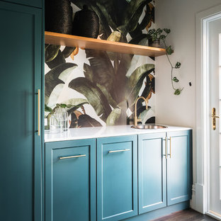 Idee per una lavanderia multiuso tradizionale di medie dimensioni con lavello da incasso, ante in stile shaker, top in quarzo composito, pareti bianche, parquet scuro, lavatrice e asciugatrice nascoste, pavimento marrone, top bianco e ante blu