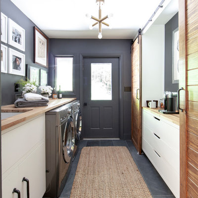 Inspiration for a country gray floor and slate floor laundry room remodel in Charlotte with an undermount sink, flat-panel cabinets, wood countertops, gray walls, a side-by-side washer/dryer, beige countertops and white cabinets