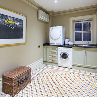 Idées déco pour une buanderie linéaire victorienne dédiée avec un évier 1 bac, des portes de placard beiges, un plan de travail en onyx, un mur beige, un sol en carrelage de céramique, des machines superposées et un placard avec porte à panneau encastré.