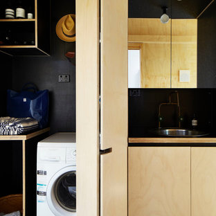 Exempel på ett litet industriellt linjärt grovkök, med skåp i ljust trä, laminatbänkskiva, svarta väggar, betonggolv, en nedsänkt diskho, luckor med infälld panel, tvättmaskin och torktumlare byggt in i ett skåp och grått golv