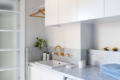 Inspiration for a small modern galley porcelain tile and beige floor dedicated laundry room remodel in Melbourne with a drop-in sink, flat-panel cabinets, white cabinets, marble countertops, white walls, a side-by-side washer/dryer and white countertops