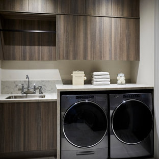 Exemple d'une buanderie linéaire chic dédiée et de taille moyenne avec un évier encastré, un placard à porte plane, des portes de placard marrons, un plan de travail en quartz modifié, une crédence blanche, une crédence en quartz modifié, un mur blanc, un sol en carrelage de porcelaine, des machines côte à côte, un sol blanc et un plan de travail blanc.
