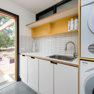 Contemporary single-wall utility room in Canberra - Queanbeyan with a drop-in sink, flat-panel cabinets, white cabinets, white walls, concrete floors, a stacked washer and dryer, grey floor and white benchtop.