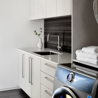 Ispirazione per una lavanderia minimalista con lavello sottopiano, ante lisce, ante grigie, pareti nere, lavatrice e asciugatrice affiancate, pavimento nero e top bianco