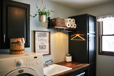 Inspiration for a mid-sized industrial single-wall linoleum floor and beige floor dedicated laundry room remodel in Other with an utility sink, shaker cabinets, black cabinets, wood countertops, blue walls, a side-by-side washer/dryer and brown countertops