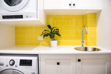 Kleine Moderne Waschküche in L-Form mit Einbauwaschbecken, Schrankfronten im Shaker-Stil, weißen Schränken, Quarzwerkstein-Arbeitsplatte, weißer Wandfarbe, Porzellan-Bodenfliesen und Waschmaschine und Trockner gestapelt in Sydney