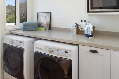 Ejemplo de cuarto de lavado lineal tradicional de tamaño medio con armarios con paneles empotrados, puertas de armario blancas, paredes blancas, suelo de madera clara y lavadora y secadora juntas