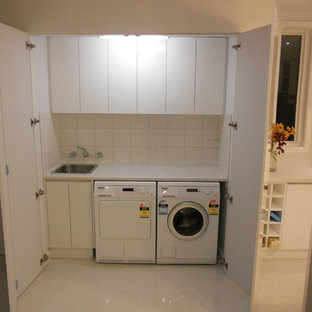 Cette photo montre une petit buanderie linéaire tendance avec un placard, un évier 1 bac, un placard à porte plane, des portes de placard blanches, un plan de travail en stratifié, un mur blanc, un sol en carrelage de porcelaine et des machines côte à côte.