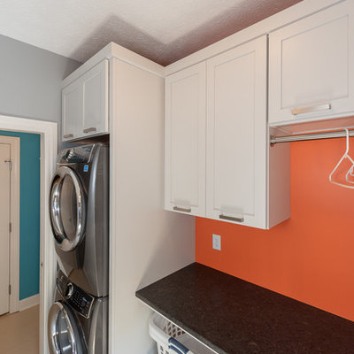 Inspiration for a small timeless single-wall ceramic tile and white floor utility room remodel in Indianapolis with recessed-panel cabinets, gray cabinets, granite countertops, gray walls, a stacked washer/dryer and black countertops