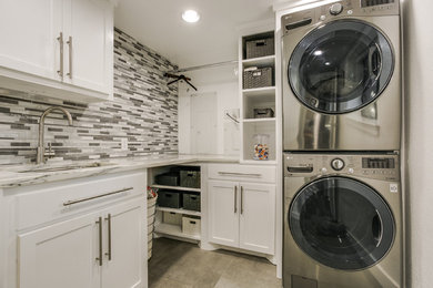 Trendy l-shaped gray floor laundry room photo in Dallas with an undermount sink, shaker cabinets, white cabinets, quartzite countertops, gray walls and a stacked washer/dryer
