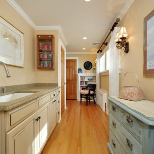 Idée de décoration pour une grand buanderie parallèle champêtre multi-usage avec un évier encastré, un placard avec porte à panneau surélevé, des portes de placard beiges, un plan de travail en granite, un mur beige, un sol en bois brun, des machines côte à côte, un sol marron, une crédence grise, une crédence en lambris de bois et du lambris de bois.