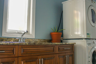Immagine di una piccola lavanderia rustica con lavello da incasso, ante con bugna sagomata, ante in legno scuro, top in laminato, pavimento in laminato e lavatrice e asciugatrice a colonna