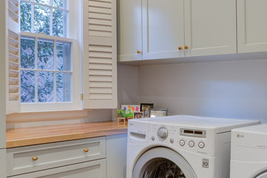 他の地域にあるトランジショナルスタイルのおしゃれな洗濯室 (L型、落し込みパネル扉のキャビネット、グレーのキャビネット、木材カウンター、白い壁、無垢フローリング、左右配置の洗濯機・乾燥機、茶色い床、茶色いキッチンカウンター) の写真