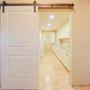 Immagine di una grande sala lavanderia classica con lavello sottopiano, ante con bugna sagomata, ante bianche, top in quarzite, pareti beige, pavimento in travertino, lavatrice e asciugatrice affiancate e pavimento beige