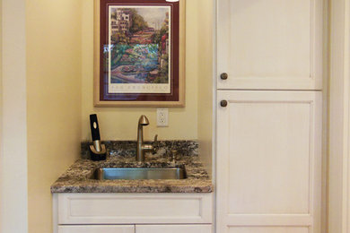 Mid-sized transitional l-shaped medium tone wood floor utility room photo in Cincinnati with an undermount sink, shaker cabinets, white cabinets, yellow walls, a stacked washer/dryer and granite countertops