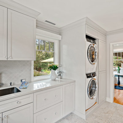 Mid-sized elegant single-wall ceramic tile and gray floor utility room photo in San Francisco with an undermount sink, shaker cabinets, white cabinets, quartz countertops, gray backsplash, ceramic backsplash, white walls, a stacked washer/dryer and white countertops