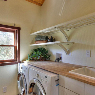 Exemple d'une petit buanderie linéaire nature avec un placard, des portes de placard blanches, un plan de travail en bois, un mur jaune, des machines côte à côte, un plan de travail beige, un placard à porte plane et un évier posé.