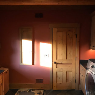Réalisation d'une buanderie tradition en L et bois dédiée et de taille moyenne avec un évier de ferme, un placard à porte shaker, des portes de placard marrons, un plan de travail en granite, une crédence verte, une crédence en bois, un mur vert, un sol en ardoise, des machines côte à côte, un sol marron, un plan de travail noir et un plafond en poutres apparentes.
