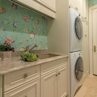 Immagine di una grande sala lavanderia classica con lavello sottopiano, pareti multicolore, pavimento in travertino, lavatrice e asciugatrice a colonna, ante con riquadro incassato e ante beige