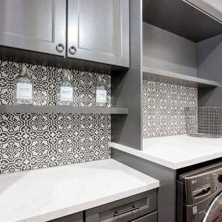 Immagine di una piccola sala lavanderia tradizionale con ante in stile shaker, ante grigie, top in quarzo composito, paraspruzzi multicolore, paraspruzzi in gres porcellanato, pareti grigie, pavimento in gres porcellanato, lavatrice e asciugatrice affiancate, pavimento marrone e top bianco