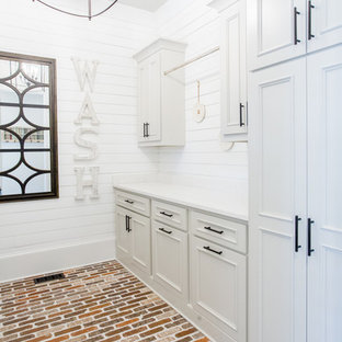Idee per una grande lavanderia multiuso chic con lavello stile country, ante con bugna sagomata, ante grigie, top in quarzo composito, pareti bianche, pavimento in mattoni, lavatrice e asciugatrice affiancate, pavimento rosso e top bianco