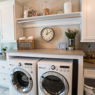 Réalisation d'une grand buanderie tradition dédiée avec un évier encastré, des portes de placard blanches, un plan de travail en quartz modifié, un mur gris, un sol en carrelage de porcelaine, des machines côte à côte et un placard avec porte à panneau encastré.