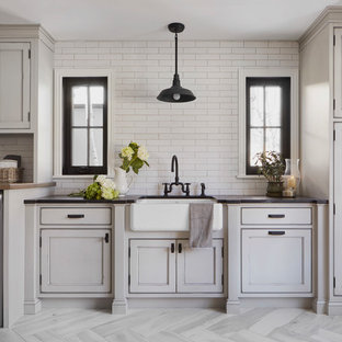 Immagine di una grande sala lavanderia country con lavello stile country, ante con riquadro incassato, ante grigie, top in saponaria, pareti bianche, pavimento in gres porcellanato, lavatrice e asciugatrice affiancate, pavimento grigio e top nero