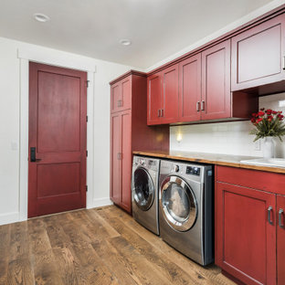 Immagine di una lavanderia multiuso country con lavello da incasso, top in legno, paraspruzzi bianco, paraspruzzi con piastrelle in ceramica, pareti bianche, pavimento in legno massello medio, lavatrice e asciugatrice affiancate, pavimento marrone, top marrone, ante in stile shaker e ante rosse