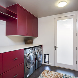 Modern inredning av en mellanstor parallell tvättstuga enbart för tvätt, med släta luckor, röda skåp, vita väggar, en tvättmaskin och torktumlare bredvid varandra, bänkskiva i koppar, klinkergolv i porslin och svart golv