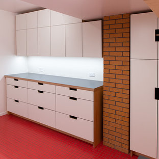 Foto på en mellanstor 60 tals grå tvättstuga, med en allbänk, släta luckor, skåp i ljust trä, laminatbänkskiva, vita väggar, klinkergolv i keramik, en tvättmaskin och torktumlare bredvid varandra och rött golv