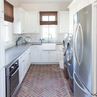 Réalisation d'une grand buanderie tradition en U multi-usage avec un évier de ferme, des portes de placard blanches, un mur beige, un sol en brique, des machines côte à côte et un placard à porte shaker.