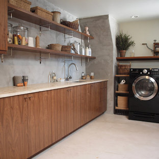 Esempio di una lavanderia multiuso minimal di medie dimensioni con ante lisce, lavatrice e asciugatrice affiancate, lavello sottopiano, ante in legno scuro, top in pietra calcarea, pareti grigie, pavimento beige e top beige