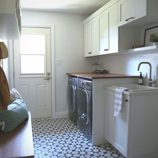 Immagine di una lavanderia multiuso scandinava di medie dimensioni con lavello da incasso, ante in stile shaker, ante bianche, top in legno, pareti bianche, pavimento in gres porcellanato, lavatrice e asciugatrice affiancate, pavimento nero e top marrone