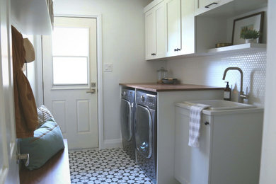 Inspiration for a mid-sized scandinavian galley porcelain tile and black floor utility room remodel in Toronto with a drop-in sink, shaker cabinets, white cabinets, wood countertops, white walls, a side-by-side washer/dryer and brown countertops
